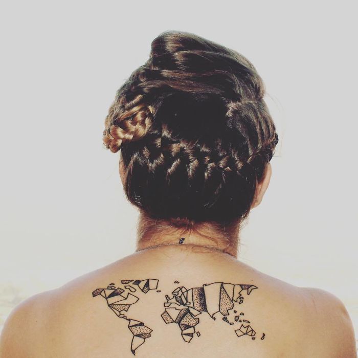 Back view of a person with a world map travel tattoo on their upper back, hair styled in an intricate updo.
