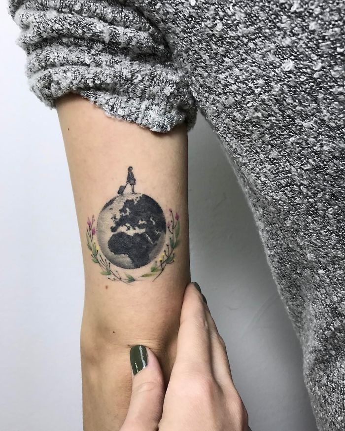 Travel tattoo of Earth with a silhouette and floral accents on a person's arm.