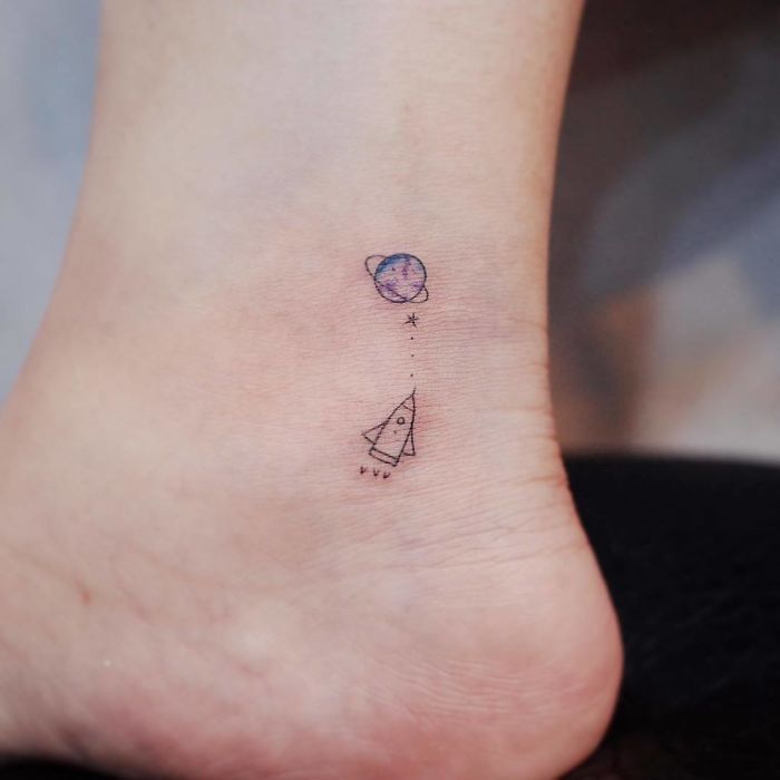 Minimalistic travel tattoo featuring a rocket and planet, inspiring wanderlust.