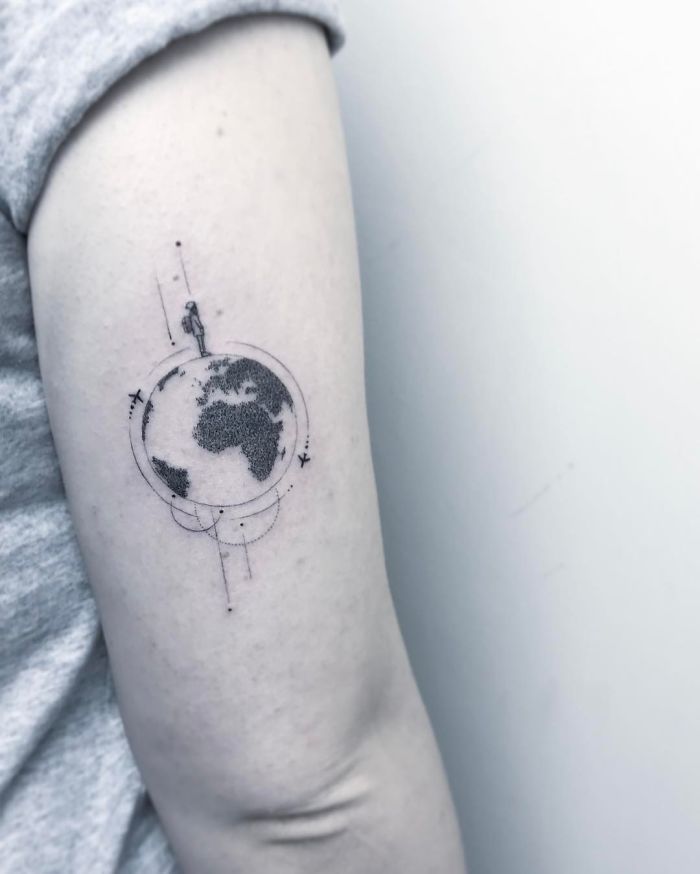 Travel tattoo of a globe on an arm, featuring continents and a small figure, symbolizing wanderlust and exploration.