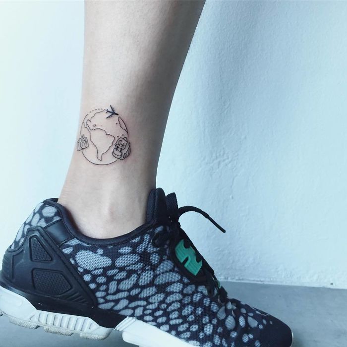 Travel tattoo with a globe and camera on an ankle, inspiring wanderlust and adventure.
