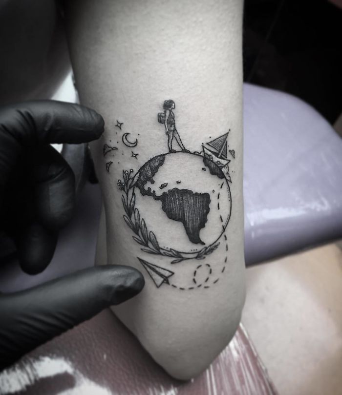 Travel tattoo featuring a traveler on a globe with paper planes and stars, inspiring adventure and wanderlust.