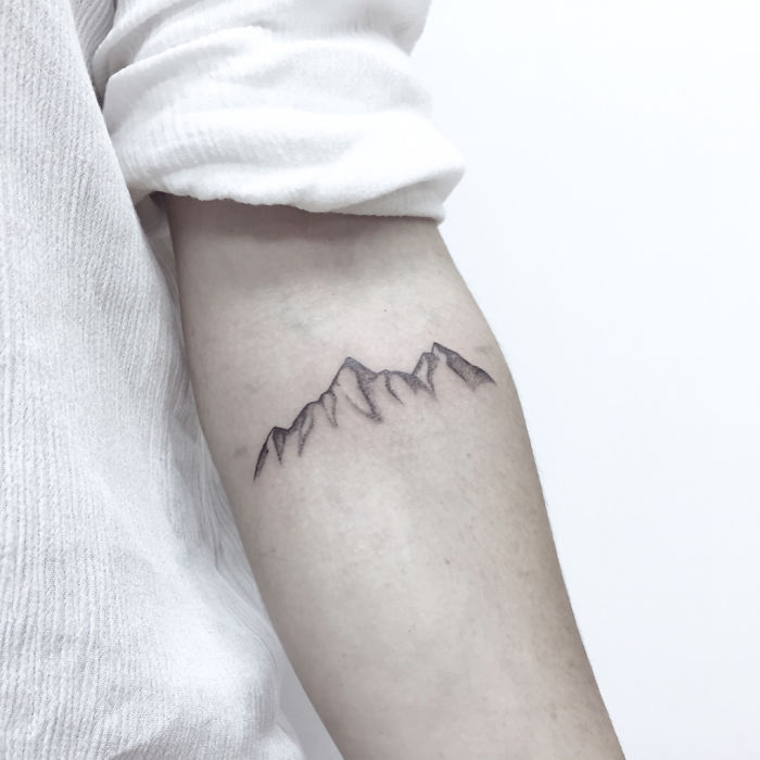 Minimalist mountain travel tattoo on inner forearm, inspiring wanderlust and adventure.
