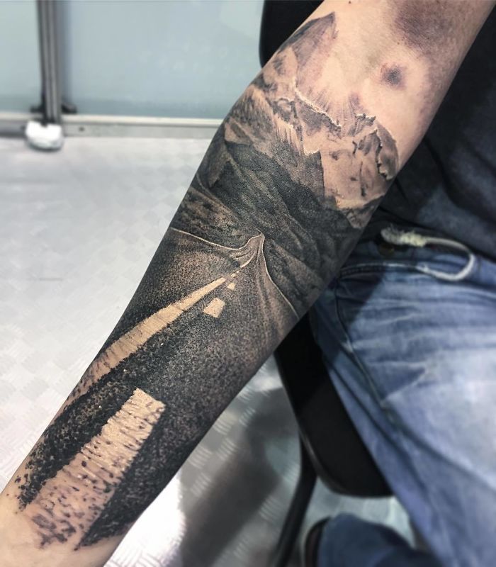 Travel tattoo depicting a scenic mountain road on a forearm, symbolizing adventure and wanderlust.