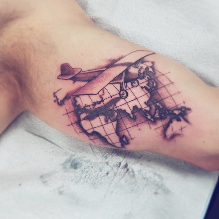 Travel tattoo of an airplane and world map on a person's arm, symbolizing adventure and wanderlust.