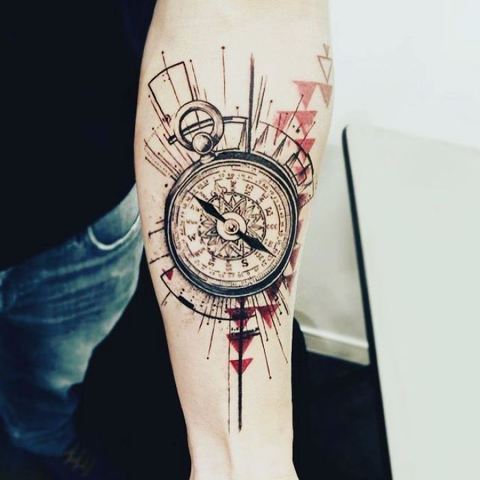 Forearm tattoo of a compass with artistic travel theme and geometric designs.