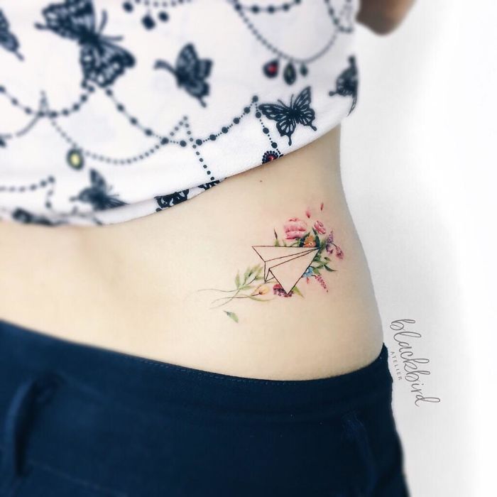 Travel tattoo of a paper airplane with flowers on a side, symbolizing adventure and wanderlust.