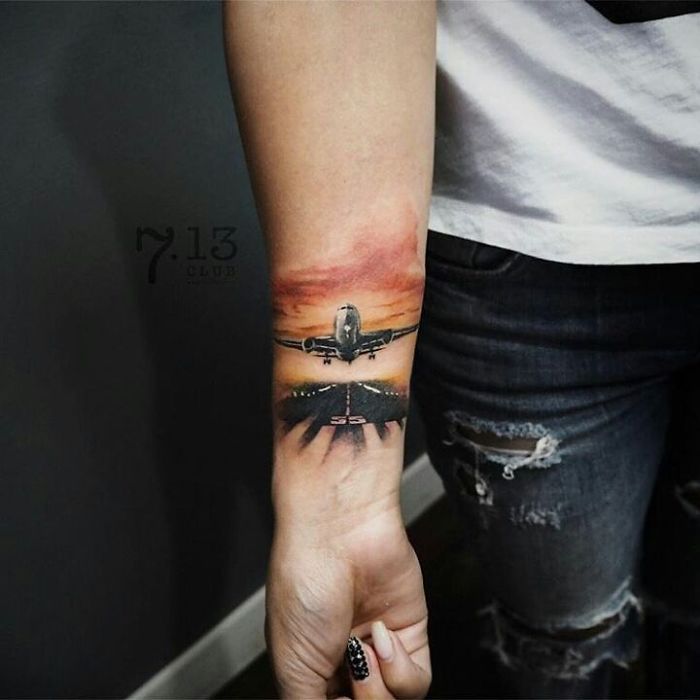 Detailed travel tattoo of a plane taking off at sunset on a person's forearm.