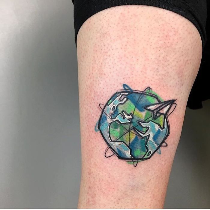 Travel tattoo of a globe and paper airplane design on an arm.