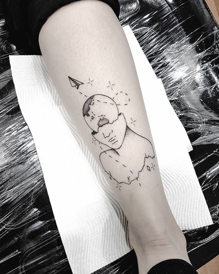 Travel tattoo of a fragmented face with a paper airplane on the leg, symbolizing wanderlust and adventure.