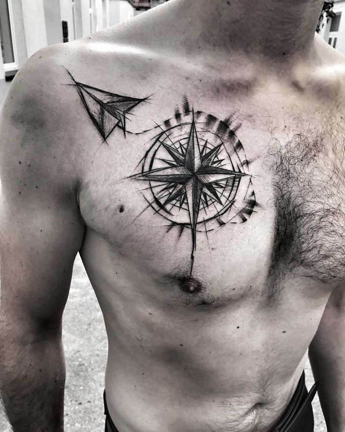 Chest tattoo of a compass and paper airplane, showcasing travel-inspired art.