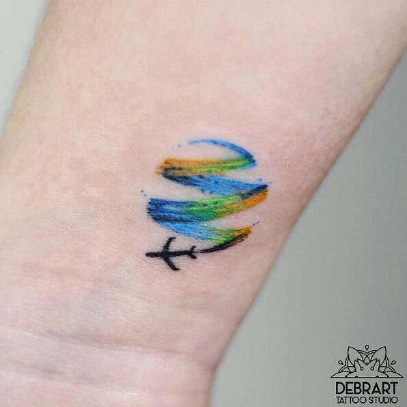 Colorful travel-themed tattoo featuring an airplane and swirling lines on forearm.