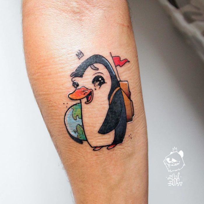 Cartoon penguin travel tattoo with a backpack and globe on arm.