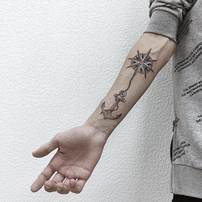 Forearm with travel tattoo featuring a compass and anchor design in black ink.