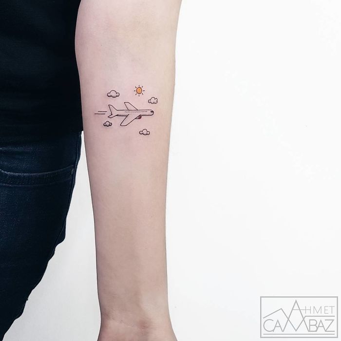 Arm with a small travel tattoo of an airplane surrounded by clouds and a sun, symbolizing travel inspiration.