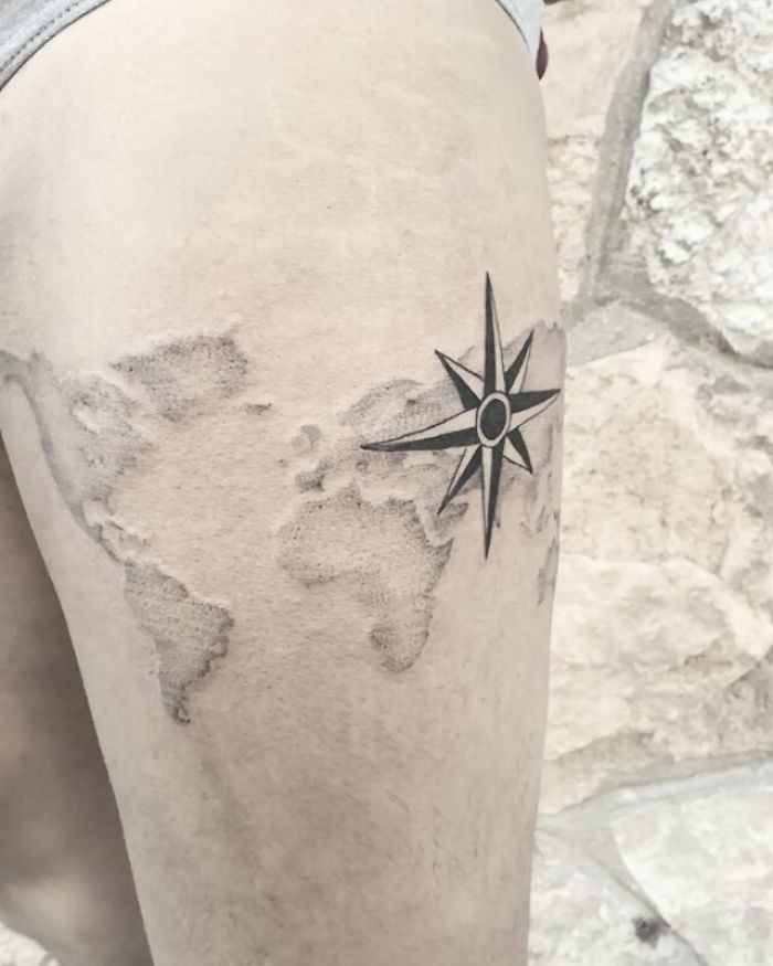 Tattoo of a world map with a compass on the thigh, inspiring wanderlust and travel exploration.