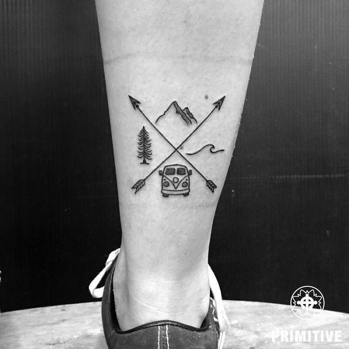 Travel tattoo with crossed arrows, mountain, tree, wave, and van design on leg.