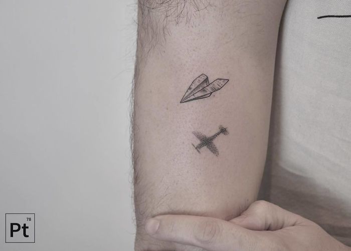 Minimalist travel tattoo featuring a paper plane and airplane on an arm.