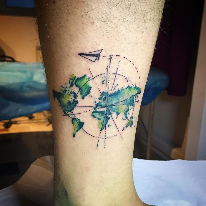 A watercolor world map travel tattoo with a paper airplane on a leg.