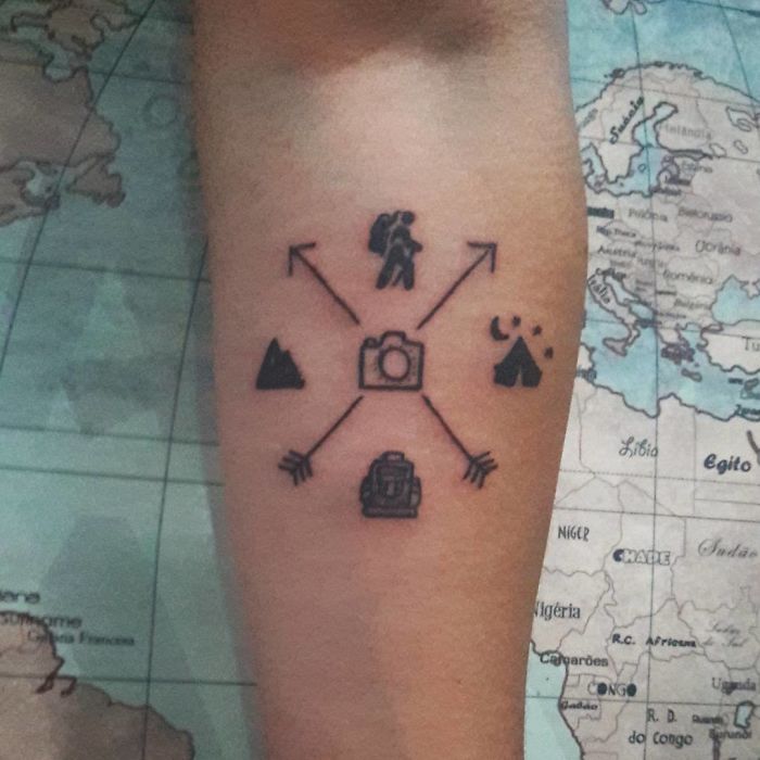 Travel tattoo with symbols of hiking, photography, and camping on an arm, over a world map background.