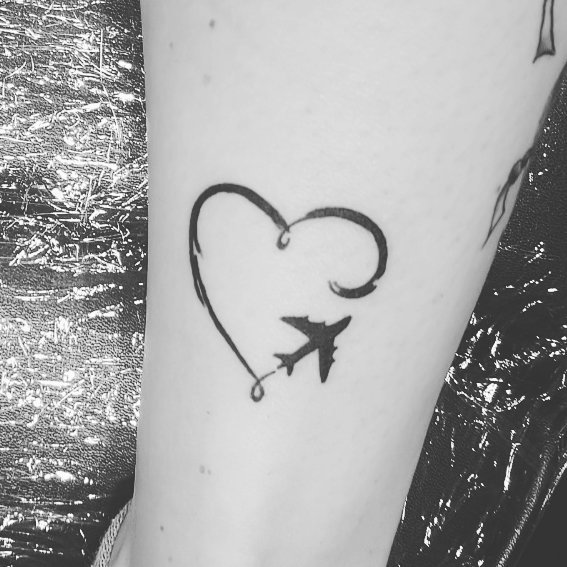 Airplane and heart-shaped line tattoo design on forearm, representing travel inspiration.