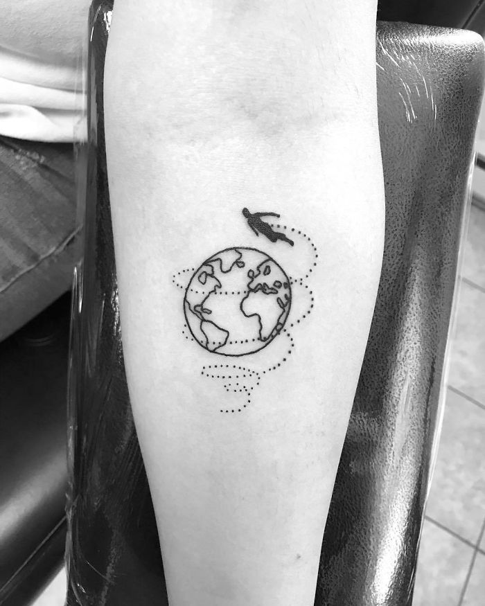 Simple travel tattoo of Earth with dotted line and airplane on forearm, inspiring wanderlust.