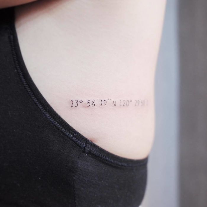 Minimalist travel tattoo with coordinates on the side of the body, suggesting wanderlust and adventure.