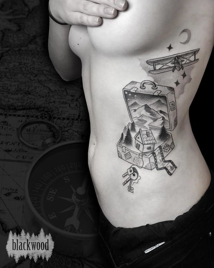 Person with travel-themed tattoo featuring a suitcase, mountains, and a plane, symbolizing wanderlust.