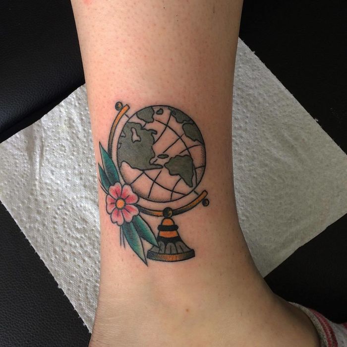 Travel tattoo featuring a globe and a flower on an ankle, symbolizing adventure and wanderlust.
