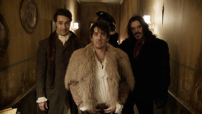 Scene from What We Do In The Shadows movie featuring three characters in period costumes and dim lighting, fun facts about movies.