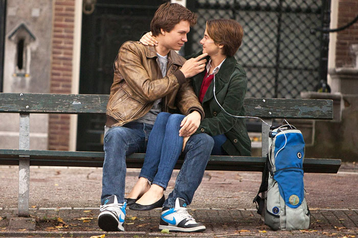 Scene from The Fault In Our Stars movie showing a young couple sharing earphones on a park bench, highlighting fun facts about movies.