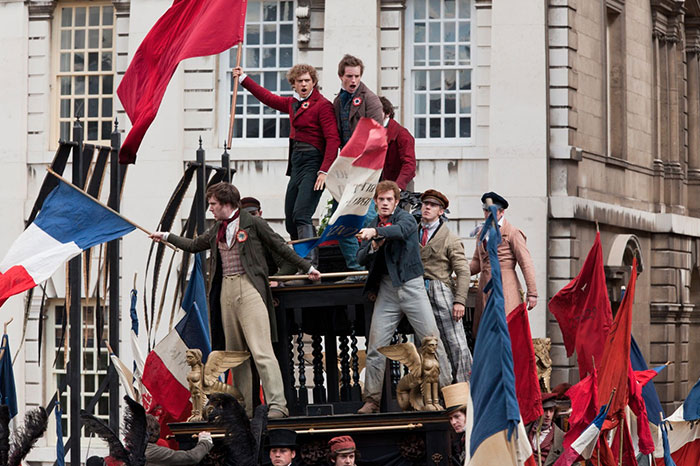 Scene from Les Misérables movie showing a revolutionary crowd waving flags, highlighting fun facts about movies.