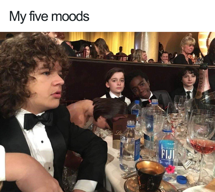 "Stranger Things" cast in tuxedos sitting at a formal event table, portraying various moods.