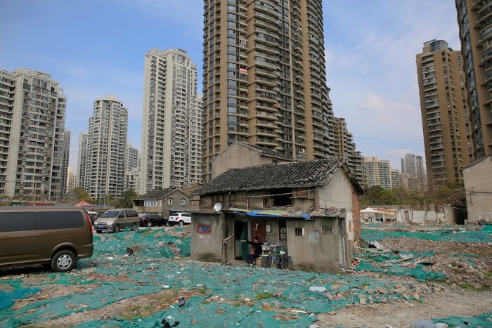 Residents Of The Guangfuli Area Of Shanghai Have Collectively Decided Not To Leave Their Homes, Creating An Entire "Nail Neighborhood." Tao Weiren Sits In Front Of His Two-Story House, Which Is Now Surrounded By High-End Condominium Buildings