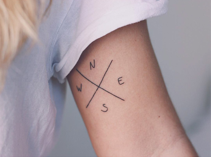 Compass travel tattoo on arm with directional letters N, S, E, W in minimalist style.
