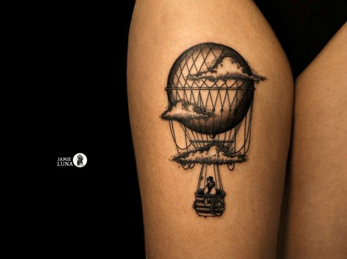 Travel tattoo of a hot air balloon with clouds, inked on a person's arm.
