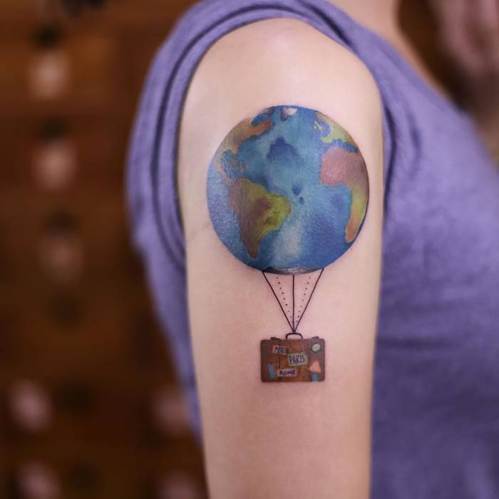 Travel tattoo of Earth and suitcase on arm inspires wanderlust.