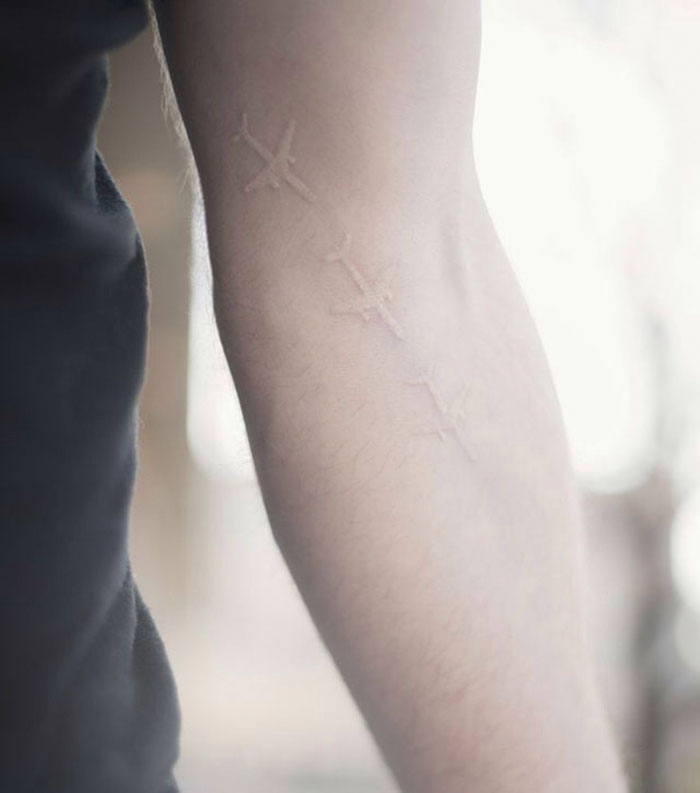 White ink tattoo featuring airplane designs on a person's arm, ideal for travel enthusiasts.