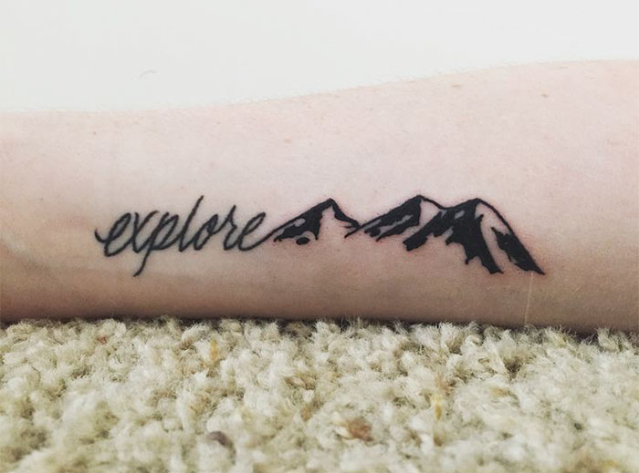 Tattoo of the word "explore" with mountain design on forearm, perfect for travel inspiration.