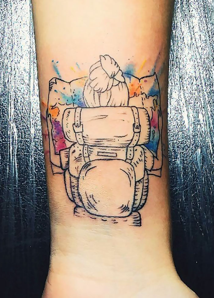 Travel tattoo of a backpacker with a map, featuring colorful watercolor accents.