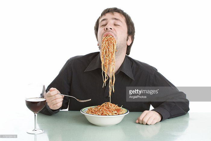 A man in a black shirt greedily eating spaghetti in e*****y
