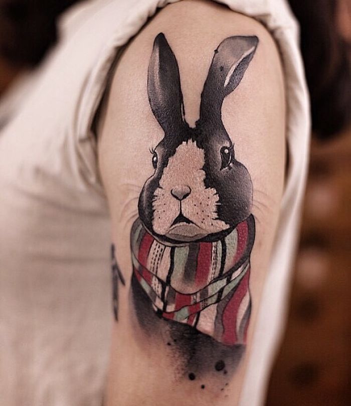 Watercolor tattoo of a rabbit with a colorful scarf on an upper arm, created by artist Chen Jie.