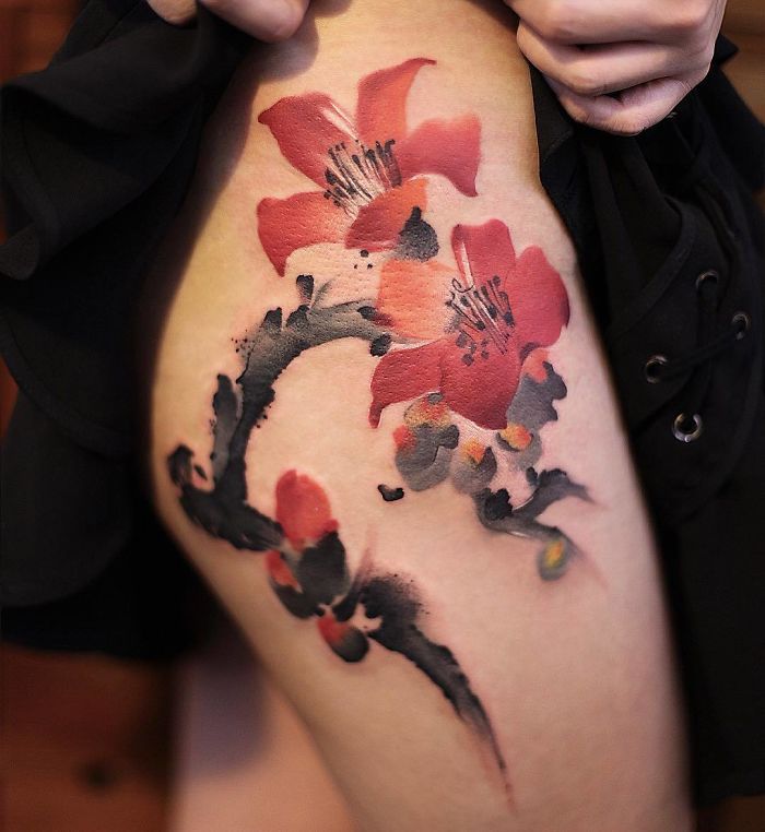 Watercolor tattoo with red floral design by Chen Jie on thigh, showcasing intricate artistry.