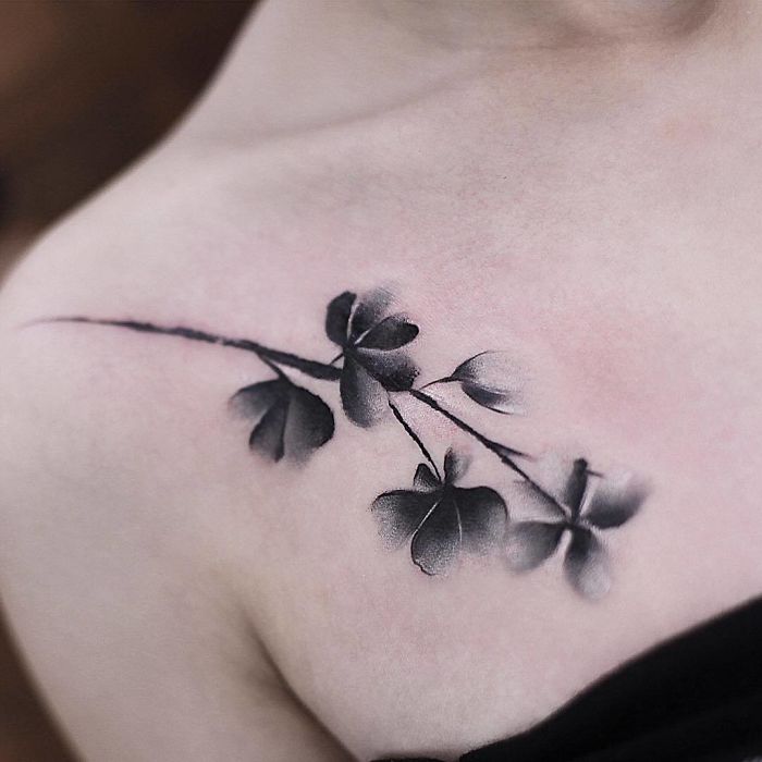 Watercolor tattoo by Chen Jie of black leaves on a person's upper chest, showcasing delicate and artistic design.