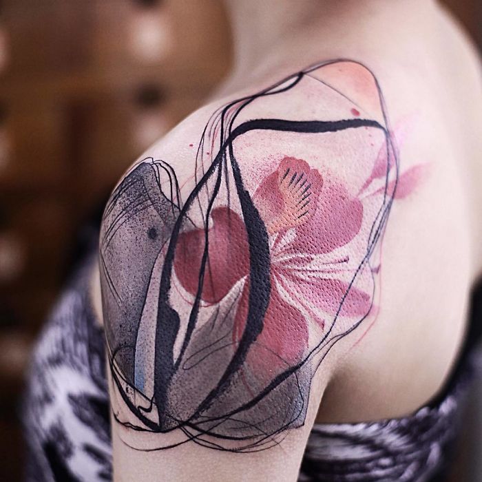 Watercolor tattoo by Chen Jie on shoulder, featuring abstract floral design with pink and black hues.