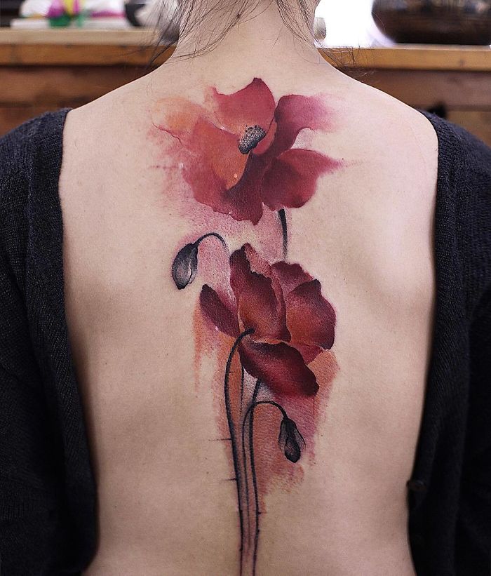 Watercolor tattoo with red flowers on woman's back, showcasing Chen Jie's artistic style.