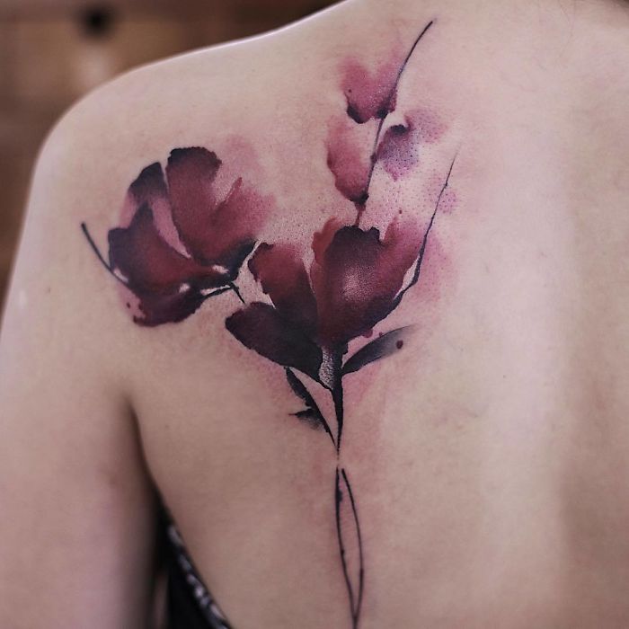 Watercolor tattoo depicting delicate red flowers on a person's back, showcasing Chen Jie's artistic style.