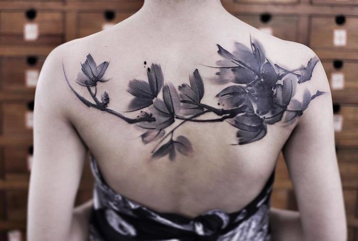 Watercolor tattoo of flowers on a woman's upper back, showcasing Chen Jie's artistic design.