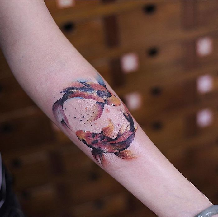 Arm with a vibrant watercolor tattoo of koi fish by Chen Jie, showcasing artistic detail and delicate colors.