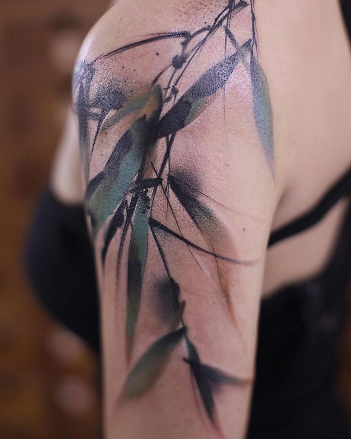 Watercolor tattoo on a shoulder, featuring abstract floral design with green and purple hues.